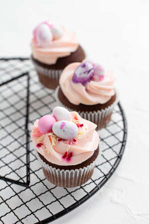 Three Easter chocolate cupcakes with caramel filling and decoration of small Easter eggs from marzipan on a round cooling rack. Selective focusの写真素材