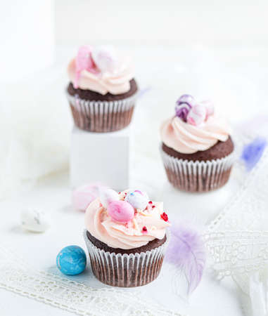 Three Easter chocolate cupcakes with caramel filling and decoration of small Easter eggs from marzipan on the white background. Selective focusの写真素材