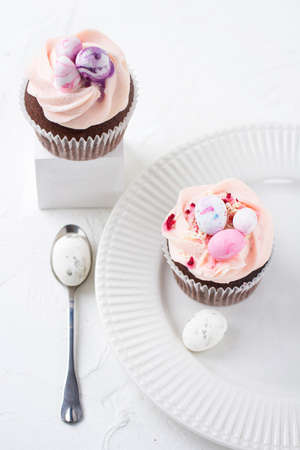 Two Easter chocolate cupcakes with caramel filling and decoration of small Easter eggs from marzipan on a white porcelain plate. Selective focusの写真素材