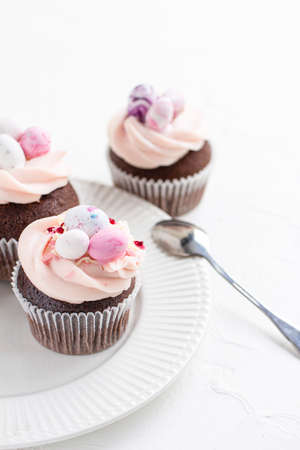 Three Easter chocolate cupcakes with caramel filling and decoration of small Easter eggs from marzipan on a white porcelain plate. Selective focusの写真素材