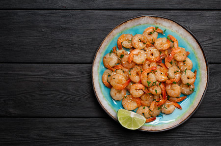 Prawns fried with garlic on a blue porcelain plate with a slice of lime on a black wooden table. Top viewの写真素材