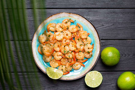 Prawns fried with garlic on a blue porcelain plate with whole and sliced limes on a black wooden table. Top viewの写真素材