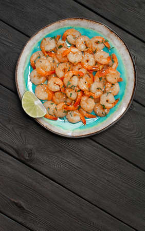 Prawns fried with garlic on a blue porcelain plate with a slice of lime on a black wooden table. Vertical photo. Top viewの写真素材