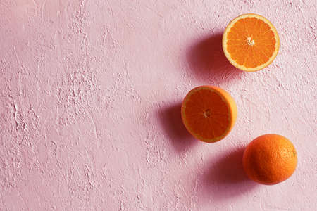 Whole and cut in half Ripe orange on a pink concrete surface. Top view. Minimalism. Copy spaceの写真素材