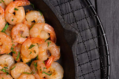 Prawns fried with garlic in a cast iron skillet on a black wooden table. Top viewの写真素材