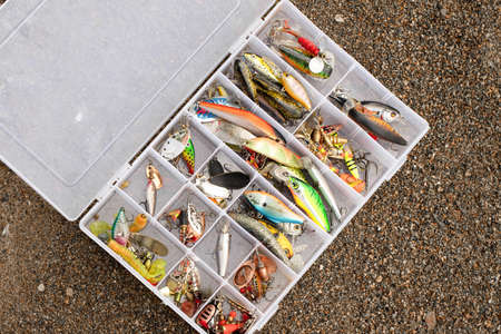A fishing tackle box filled with lures, wobblers and fishing equipment lying on the sandの写真素材