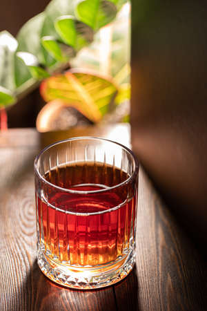 Faceted glass of whiskey on a wooden table against the background of exotic plants.の写真素材
