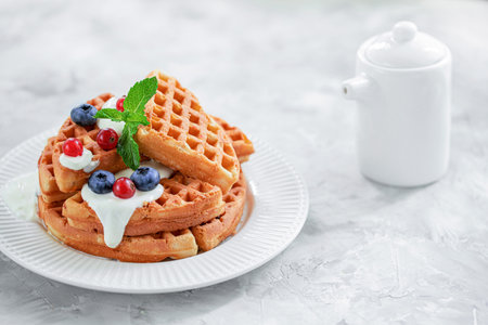 Waffles with blueberries red currants poured with yogurt on a white porcelain plate.の写真素材