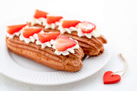 Eclairs with cream and strawberries on a white plate. Valentines Day Concept