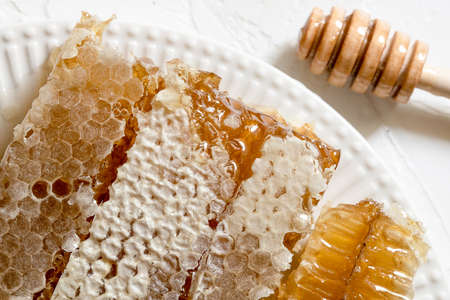 Sealed honeycomb of honey with wooden Honey Dipper for mixing and tasting natural honey on a white...