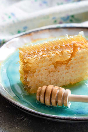 Sealed honeycomb of honey with wooden Honey Dipper for mixing and tasting natural honey on a blue porcelain plate on a white tableの写真素材