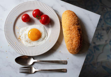 Fried eggs with cherry tomatoes and a bun with sesame on the table. Breakfast.