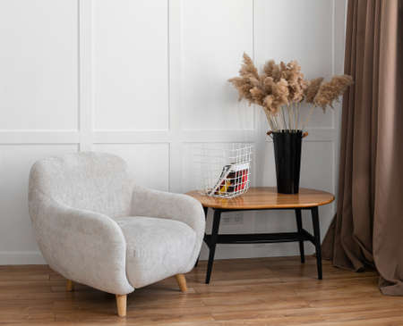 A gray armchair and a coffee table stand on a wooden floor against a white wall. Recreation area in the apartment, studio.の写真素材