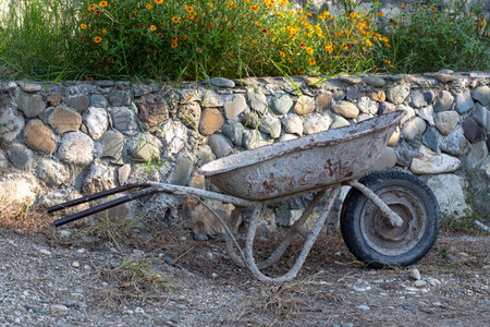 An old rusty empty wheelbarrow stands against the background of a stone wallの写真素材