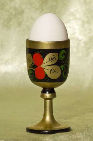 white egg in a wooden stand with a picture on a green backgroundの写真素材