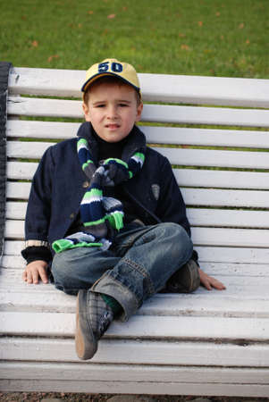 Young boy sitting on a bench in a park.の写真素材