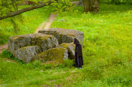 Figure in a black cloak next to enormous stone in a parkの写真素材