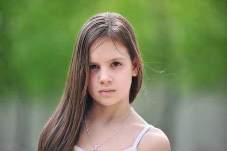 Portrait of the little girl with a serious face on a green summer backgroundの写真素材