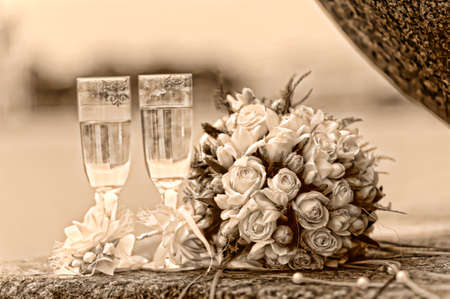 Photo of two glasses full of champagne with bridal bouquet of white roses near by. Photography done in retro styleの写真素材