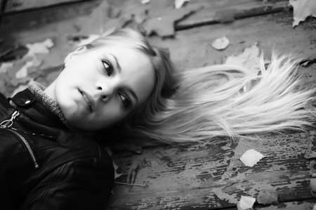 Beautiful woman with blond hair and leaves on it lying on wooden floor の写真素材