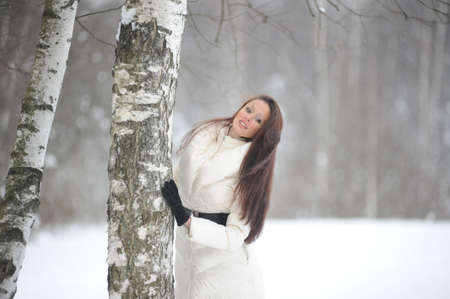 Pretty woman in a winter park standing next to a birchの写真素材