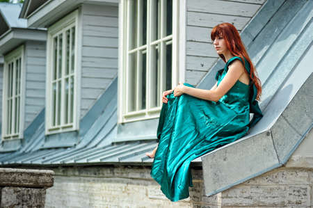 The girl in a green dress sitting on the brink of a roofの写真素材
