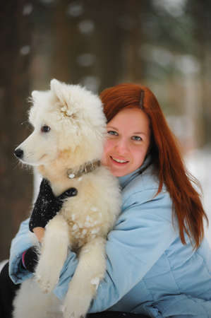 Young red-haired woman in the winter with his puppy Samoyed