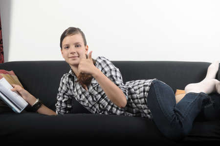 Pretty young girl reading book on sofa の写真素材
