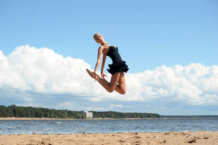 Happy healthy woman leaping on seashore on summer vacationの写真素材