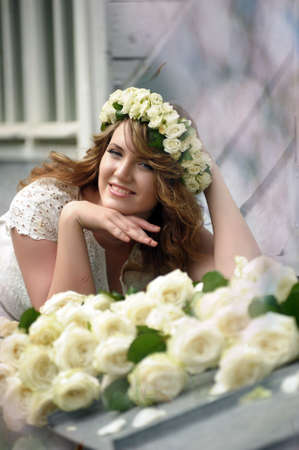 Portrait of a beautiful woman with a bouquet of white roses and a wreath on her headの写真素材