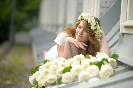 Portrait of a beautiful woman with a bouquet of white roses and a wreath on her headの写真素材