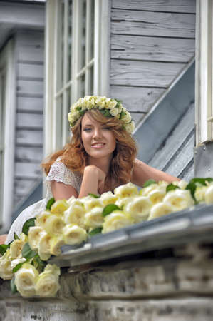 Portrait of a beautiful woman with a bouquet of white roses and a wreath on her headの写真素材