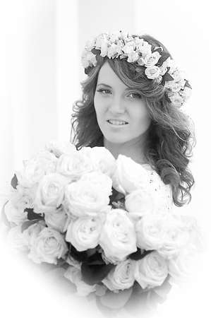 Portrait of a beautiful woman with a bouquet of white roses and a wreath on her headの写真素材