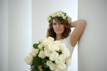 Portrait of a beautiful woman with a bouquet of white roses and a wreath on her headの写真素材