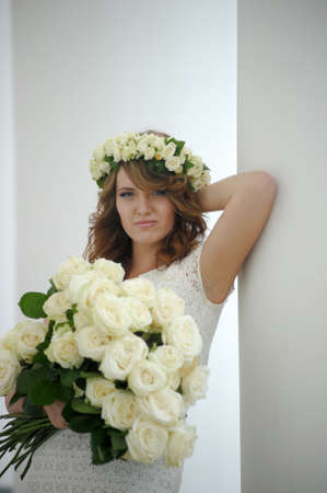 Portrait of a beautiful woman with a bouquet of white roses and a wreath on her headの写真素材