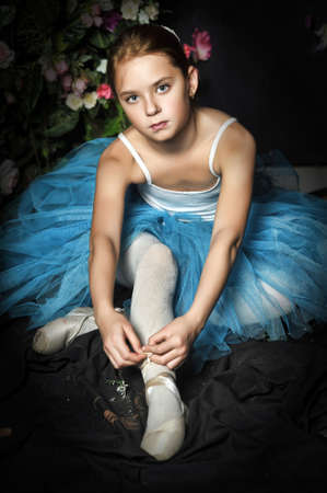 a young ballerina in a blue skirt on a floral background tying pointe shoesの写真素材