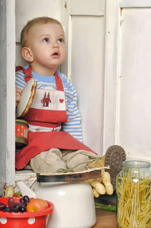 small child in an apron in the kitchen of utensilsの写真素材