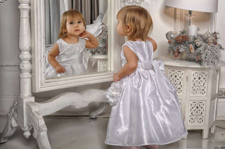 Little girl dressed admires her reflection in mirrorの写真素材