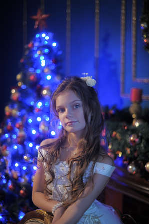 girl in white dress in the fireplace on  background glowing Christmas treeの写真素材