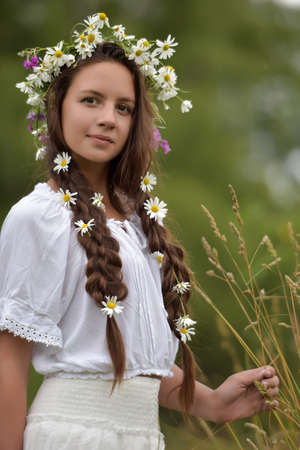 Dark-haired girl with braids and daisies in a white summer dress.の写真素材
