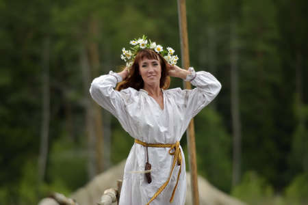 Woman in ethnic clothes with a wreath of flowers by the water on Midsummer.の写真素材