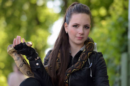 Portrait of a girl in a black leather jacket with python on her shoulders.