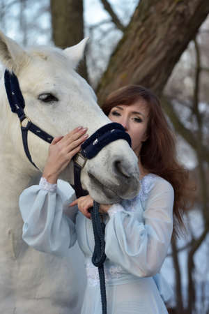 Charming brunette in pale blue dress with a white horse in the early spring.の写真素材