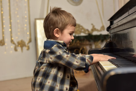 cute little boy, sitting on chair and playing on pianoの写真素材