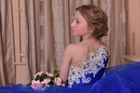 young princess in a blue dress is sitting on the bed with a bouquet of rosesの写真素材