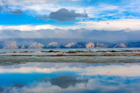 Baikal, mountains and ice on the lake, clouds reflecting in the waterの写真素材