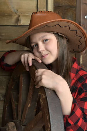 young girl cowboy in a red checkered shirt on the background of a wooden wallの写真素材
