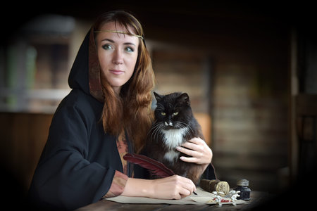 A woman in a medieval cloak sits with a pen and writes. Black cat nearの写真素材