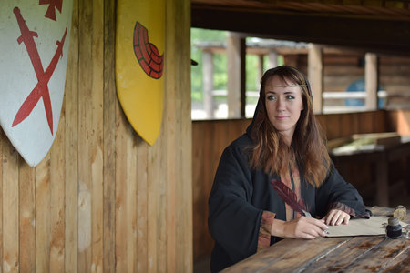 A woman in a medieval cloak sits with a pen and writes