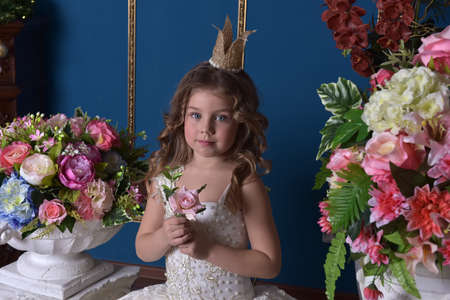 portrait of a little girl princess in a white dress and a crown among flowersの写真素材